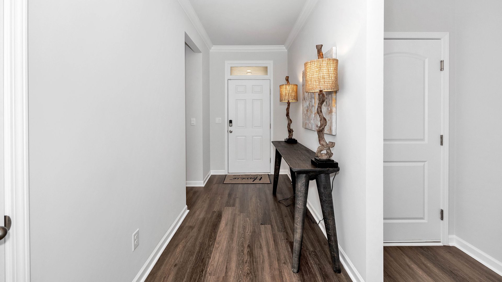 Narrow hallway with wood-look flooring and a dark console table with lamps; white doors and walls.