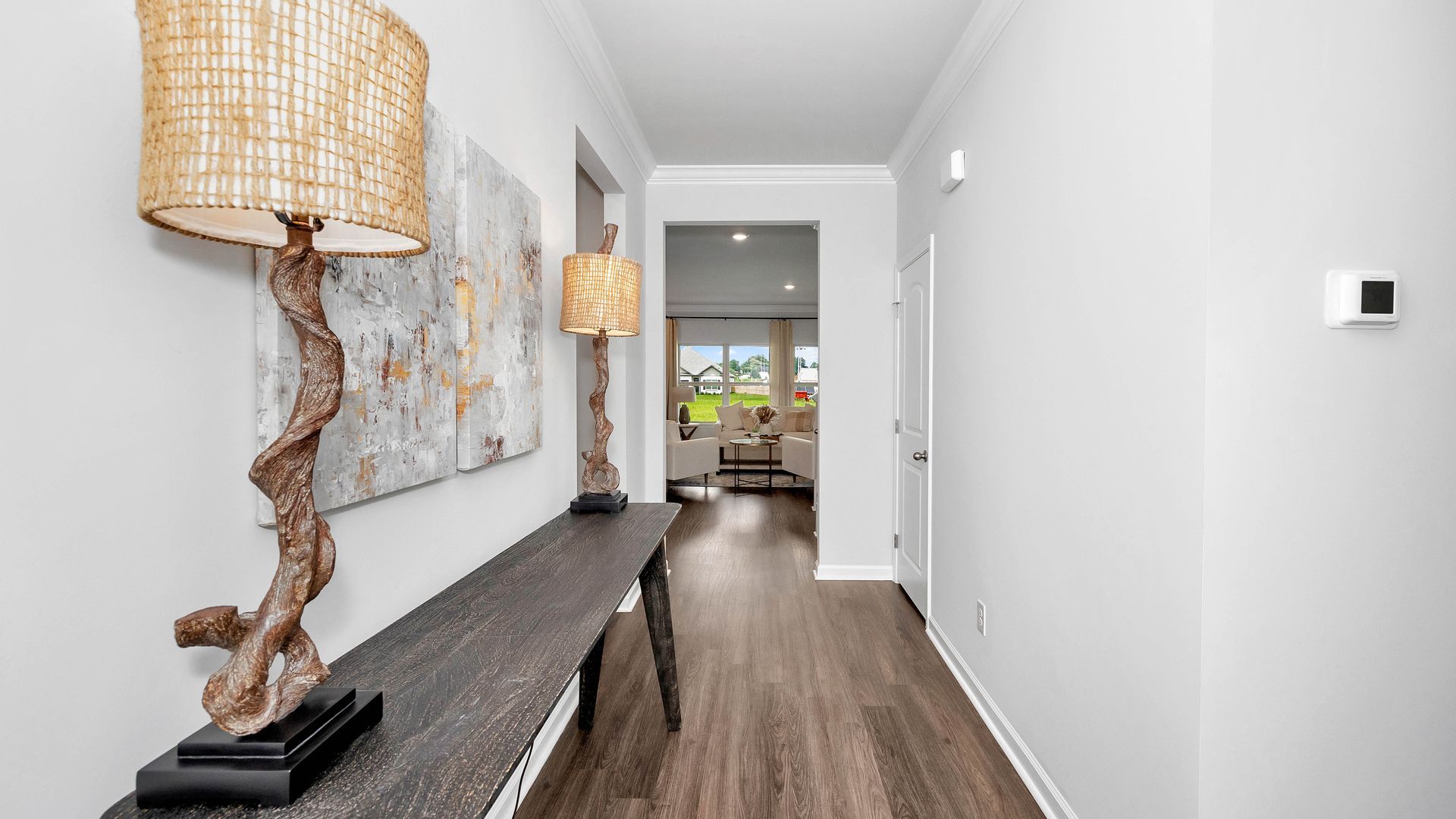 Entryway with wooden console table, lamps, and abstract art, leading to a light-filled room.