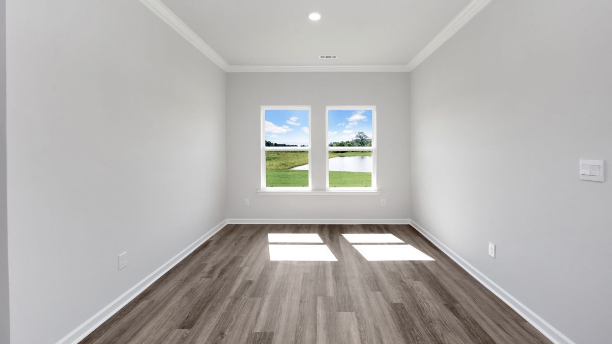 Empty room with gray walls, wood floor, and two windows overlooking a lake.