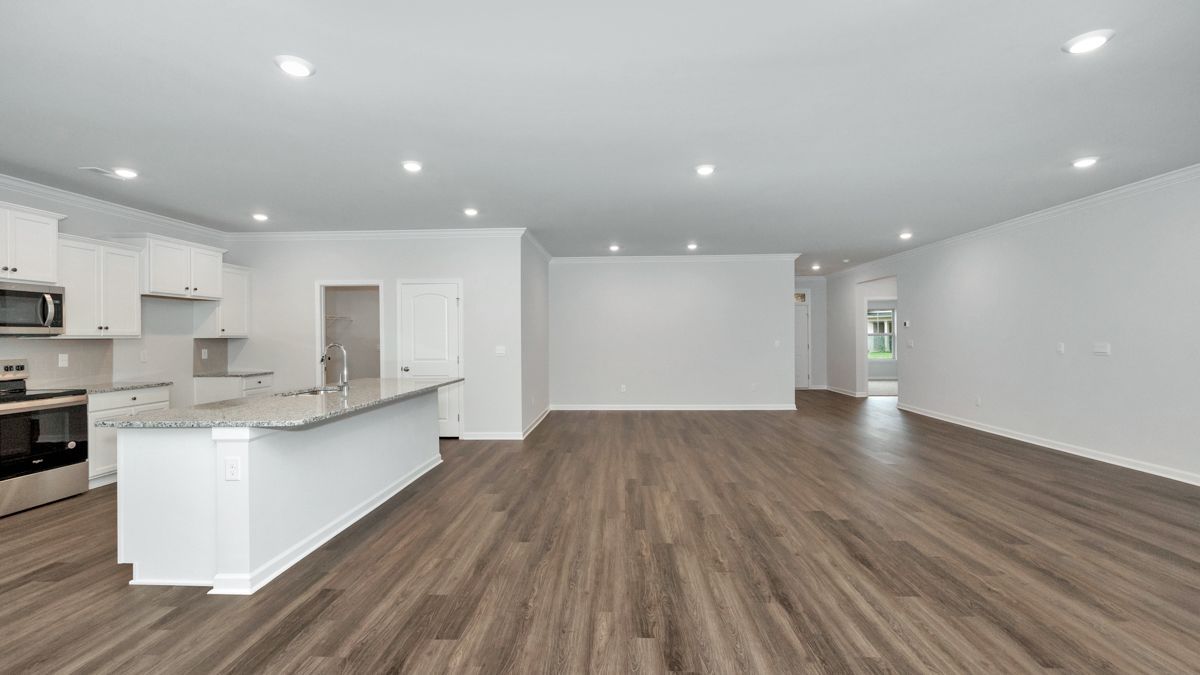 Spacious, bright, open-plan kitchen and living area with white cabinets, wood floors, and an island.