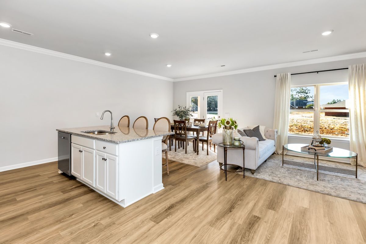 Open-concept living space with kitchen island, dining area, and living room with neutral colors and natural light.