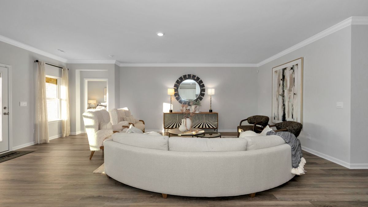 Spacious living room with a large white curved sofa, round mirror, and light gray walls.