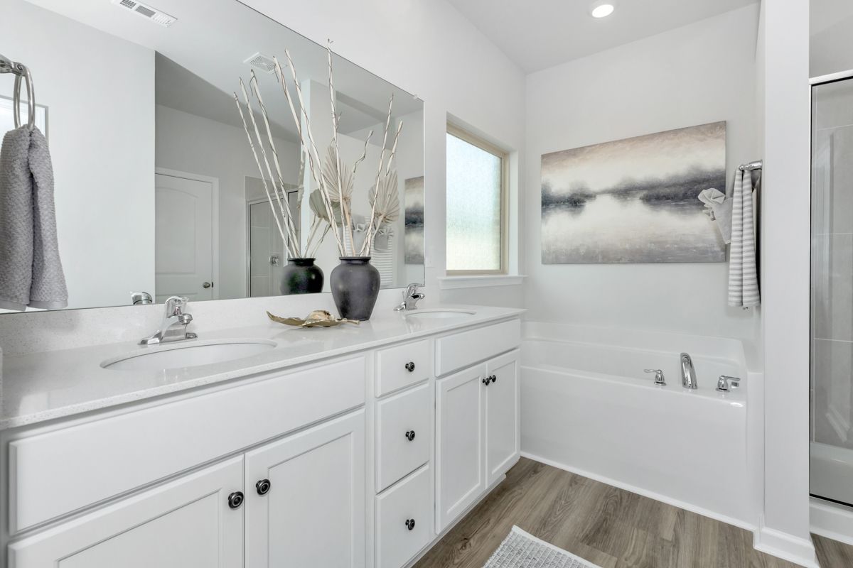 Modern white bathroom with double vanity, artwork, and a bathtub.