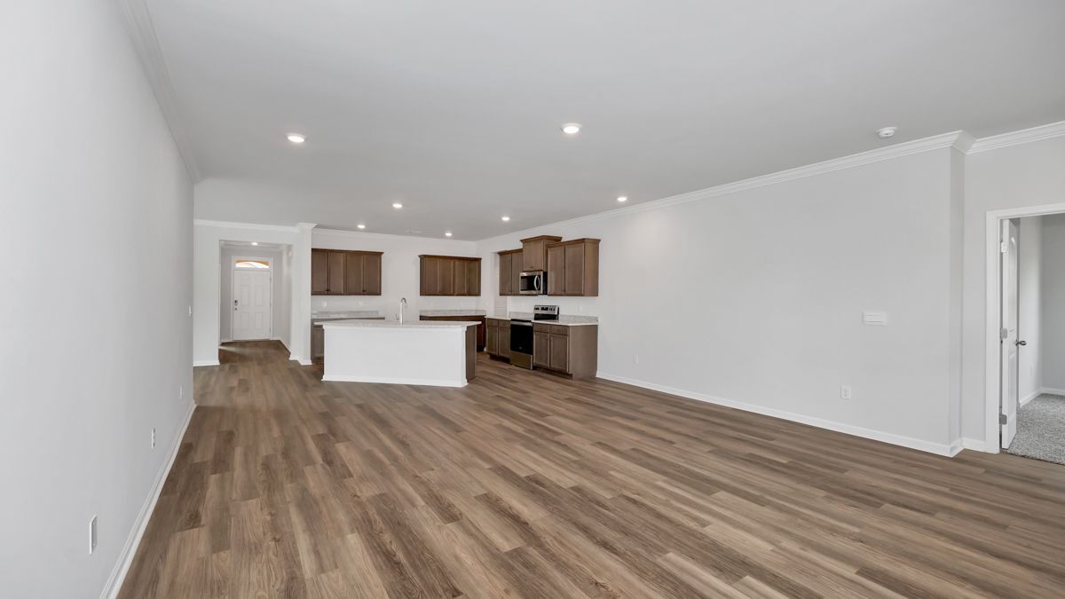 Spacious, open-concept living area with wood flooring, white walls, and a kitchen in the background.
