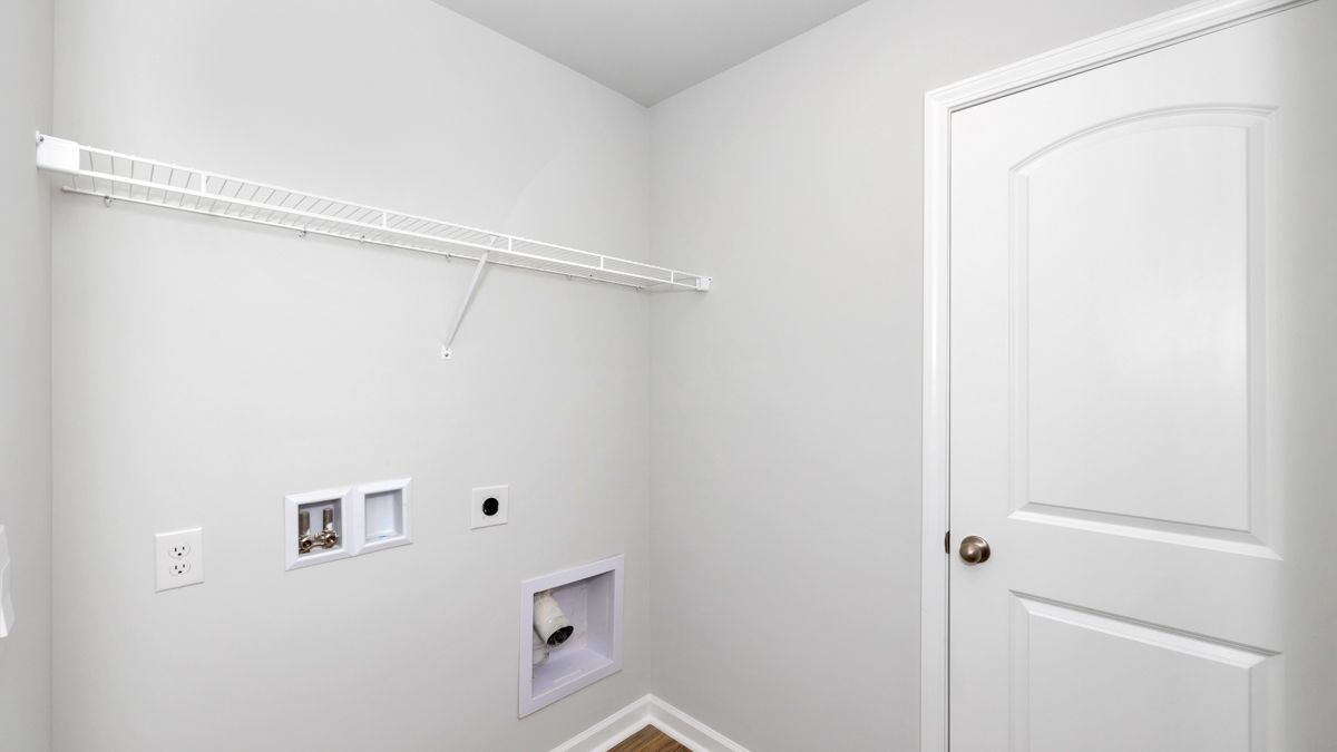 Empty laundry room with a shelf, electrical outlets, and a door. White and gray color scheme.