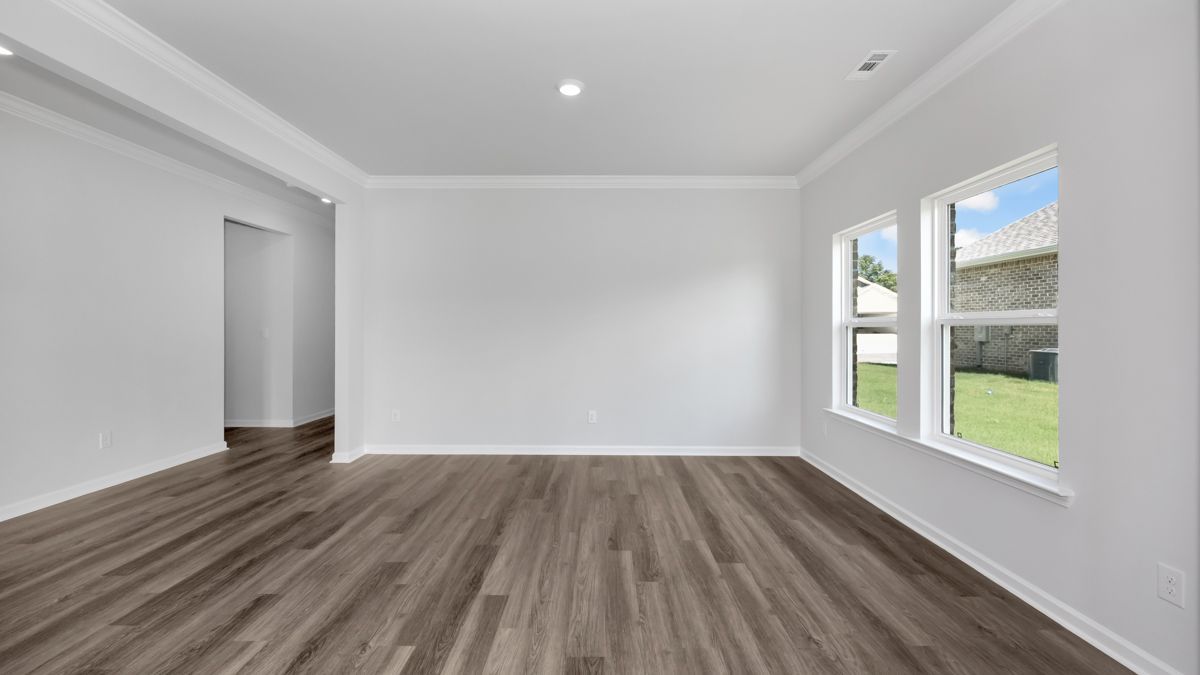 Empty room with gray wood flooring, white walls, and windows overlooking a yard.