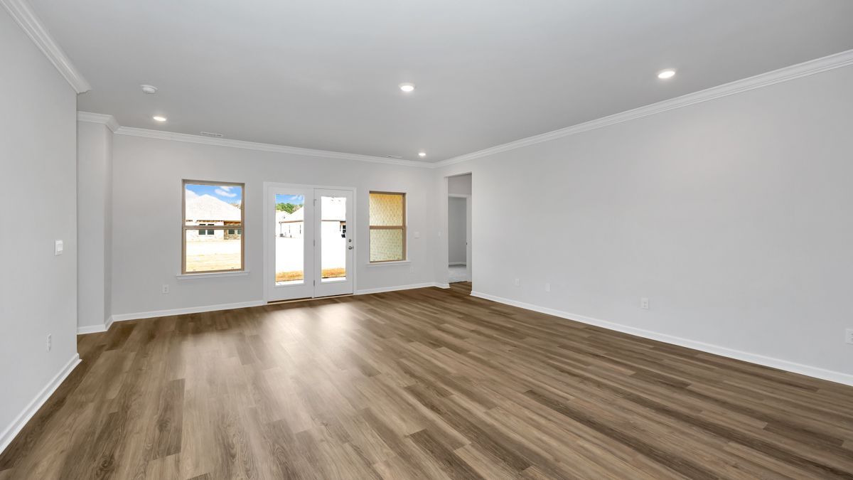 Empty room with wooden floor, white walls, and windows.
