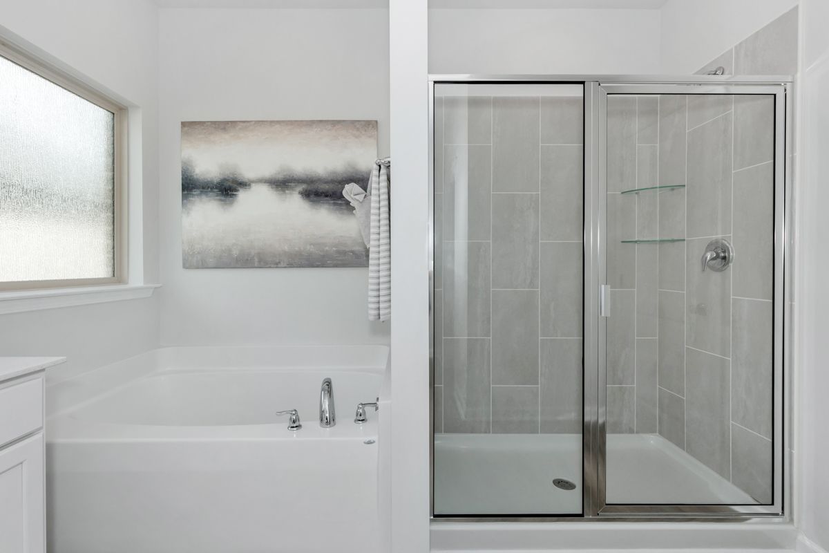 White bathroom with a tub and shower, featuring art on the wall and a frosted window.
