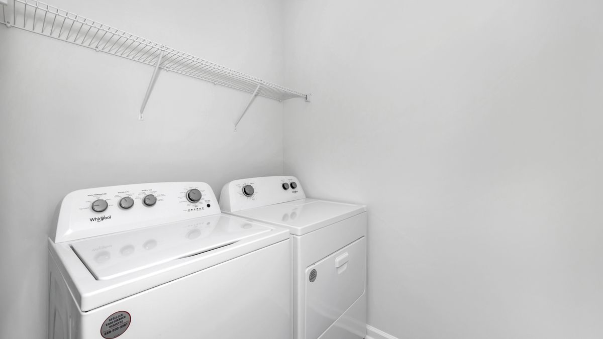 White washer and dryer in a laundry room with a shelf above.