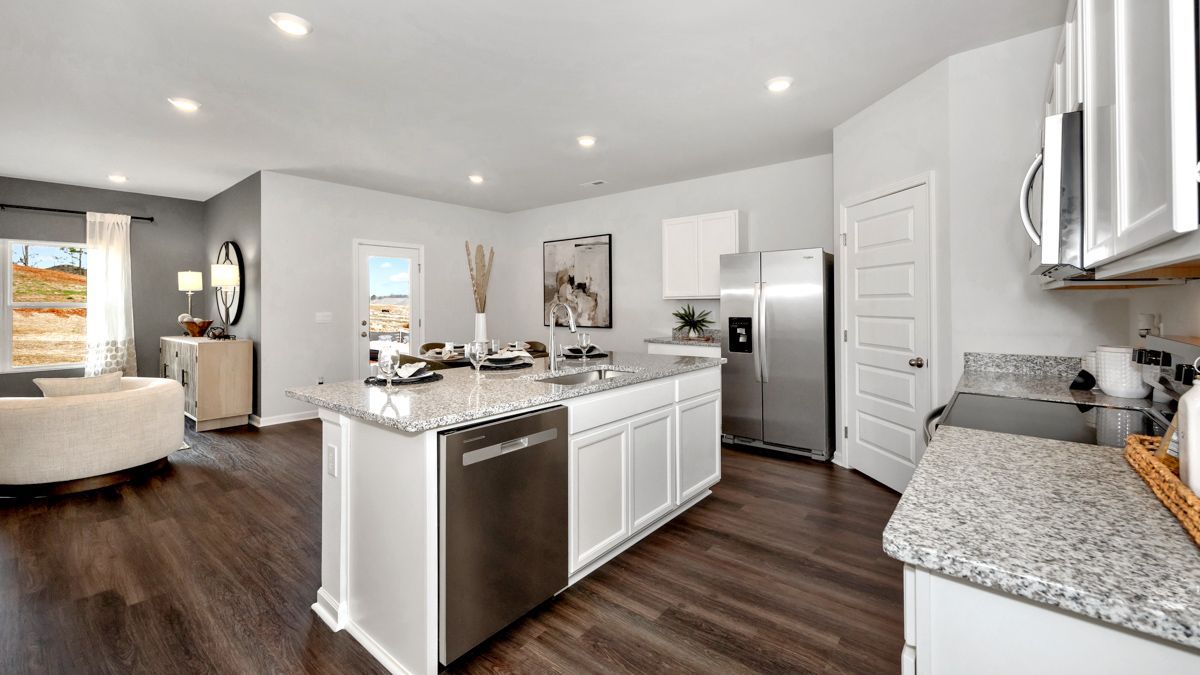 Open-concept kitchen with white cabinets, island, stainless steel appliances, and dark wood floors.