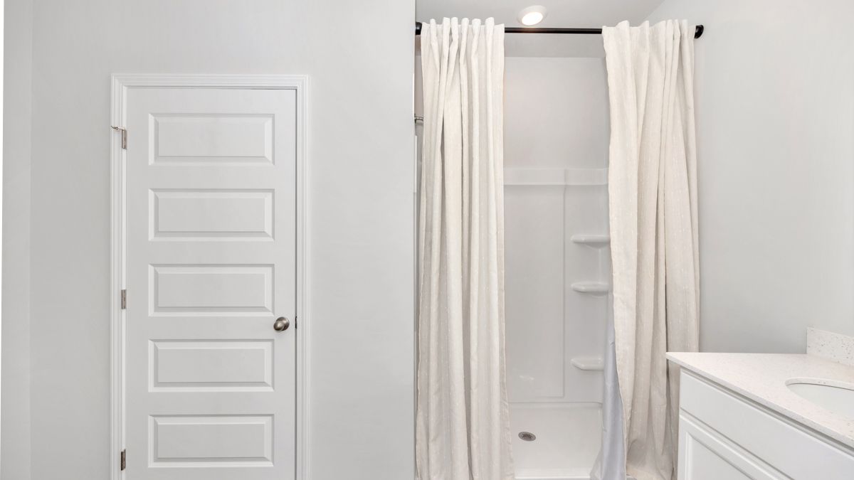 White bathroom with a closed door, shower with curtain, and a vanity.