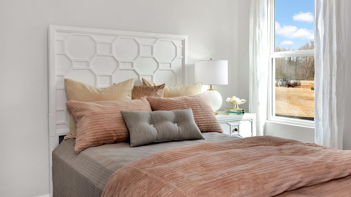 Bedroom with white geometric headboard, pink and beige pillows, and a peach comforter.