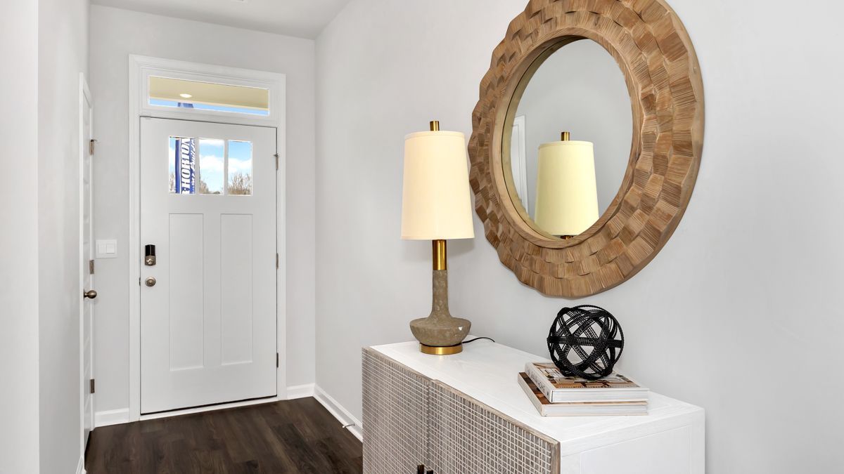 White entryway with a door and a console table. Table has lamp, mirror, and decor.