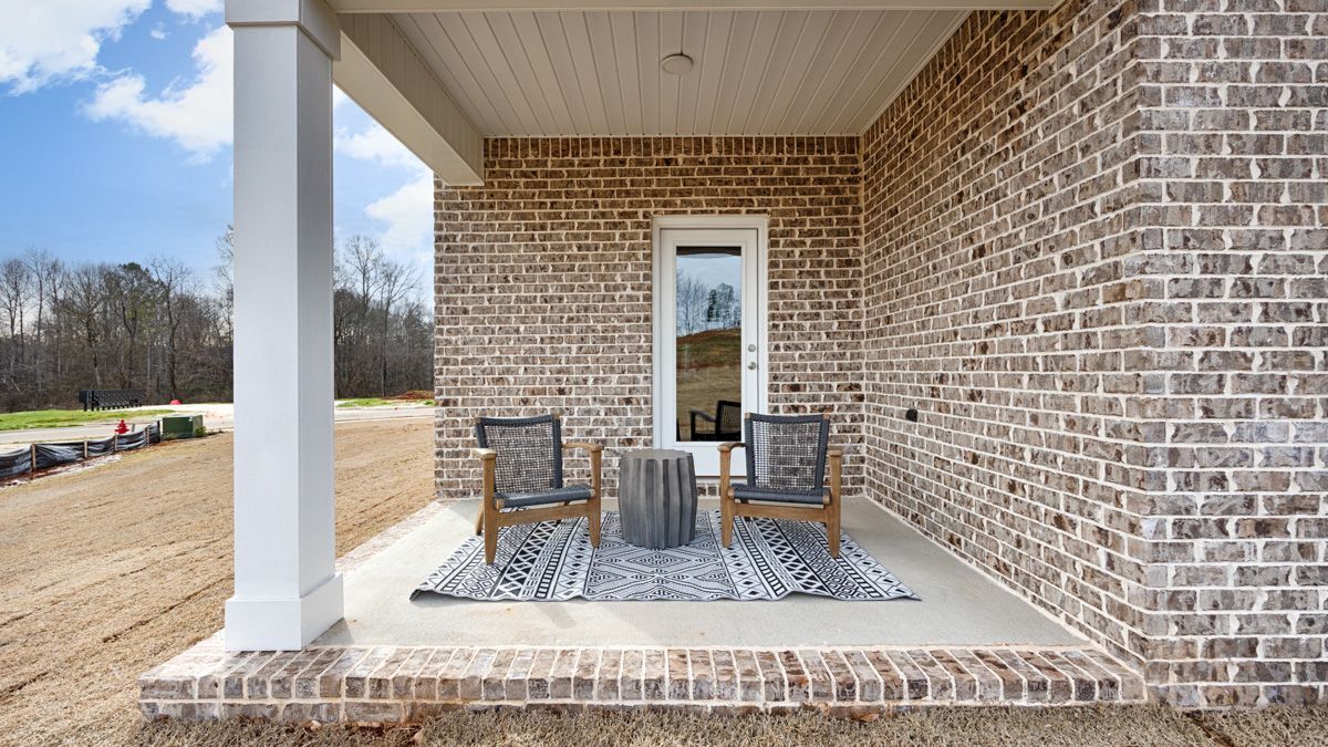 Covered brick porch with two chairs, a small table, and a door.