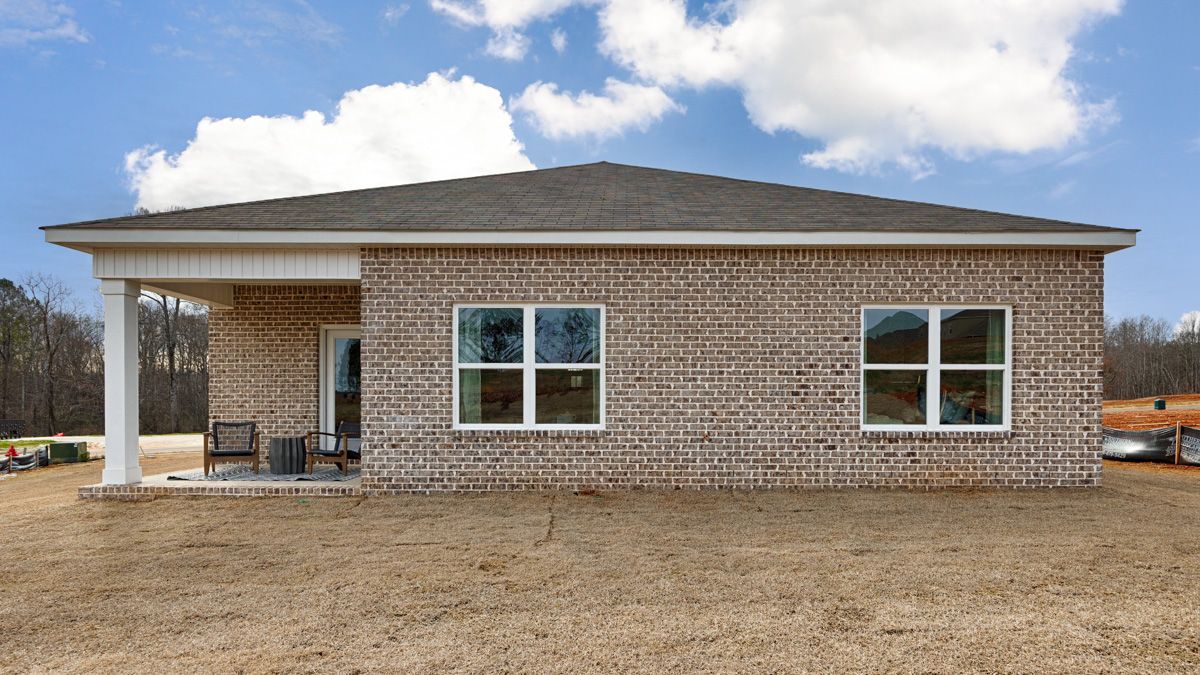 Brick house with porch and windows on brown field, blue sky.