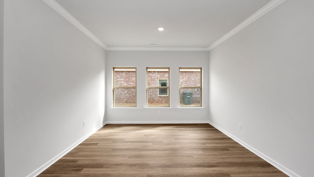 Empty room with three windows, brown wood floors, white walls and trim.