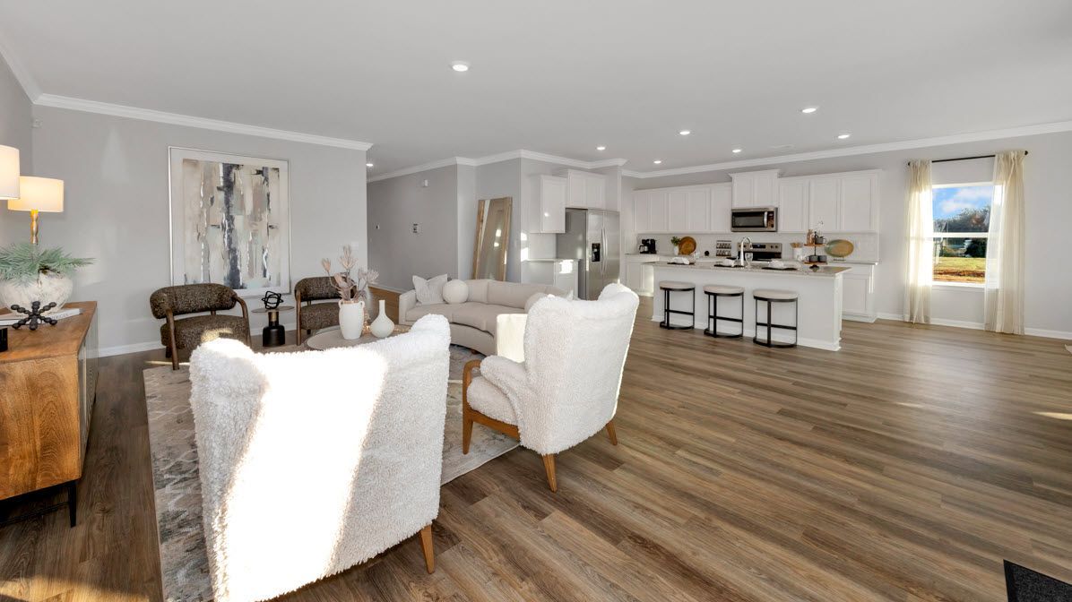 Open-concept living space with kitchen, seating area, and wood-look flooring. White walls and cabinets, neutral furniture.