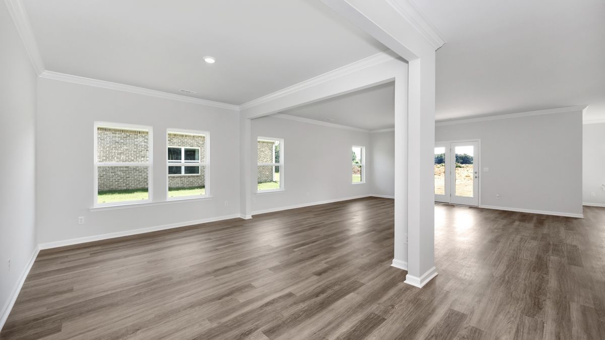 Empty, bright living room with wood-look flooring, white walls, and windows.
