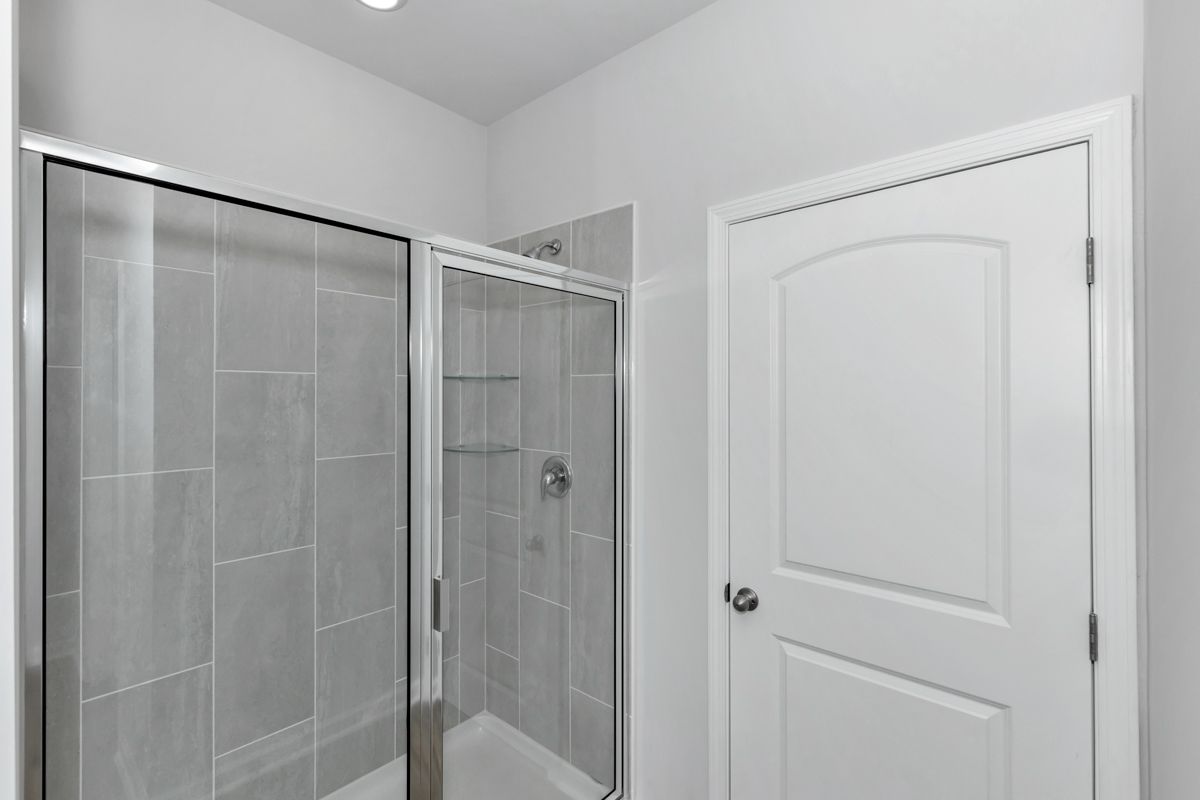 Bathroom with glass shower, white door, and gray tile walls.