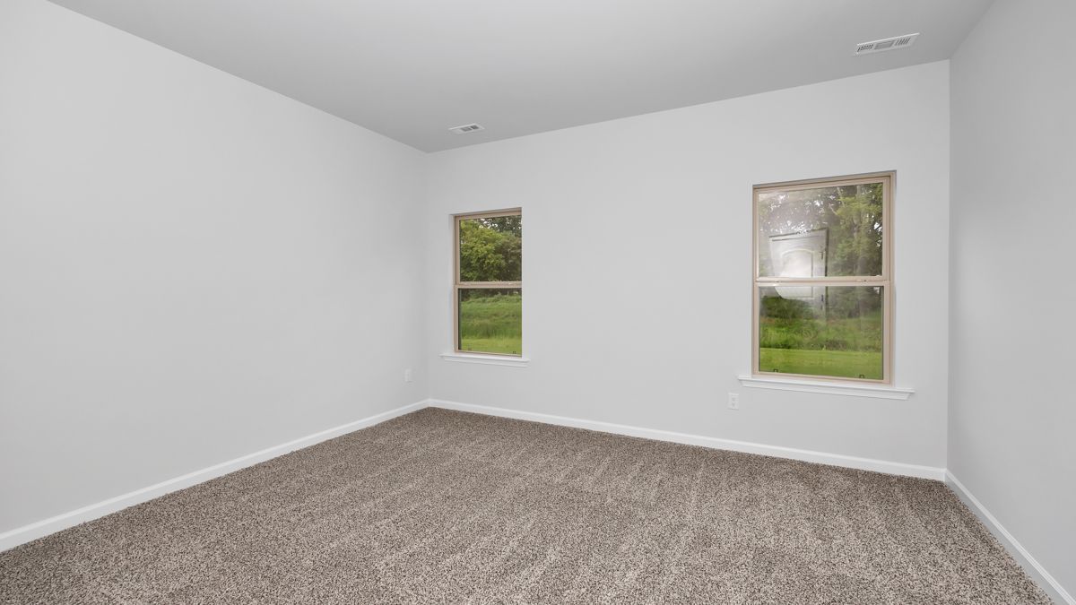 Empty room with gray carpet, white walls, and two windows overlooking greenery.