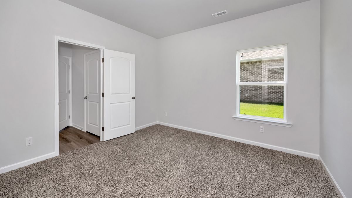 Empty room with gray walls, carpet, a white door, and a window overlooking grass.