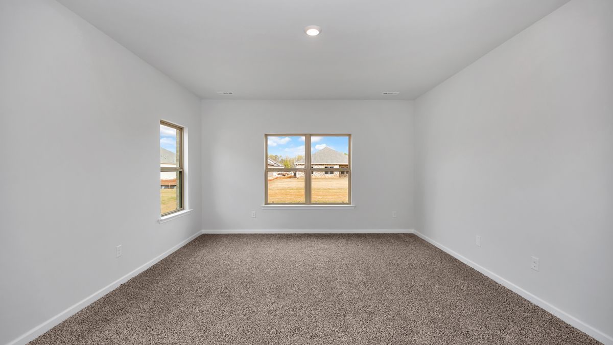 Empty room with carpet, white walls, and windows offering a view of a sunny day outside.