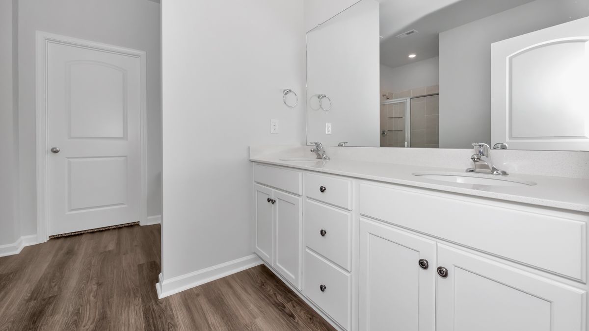 White bathroom with double vanity, light-colored countertop, and a door on the left.