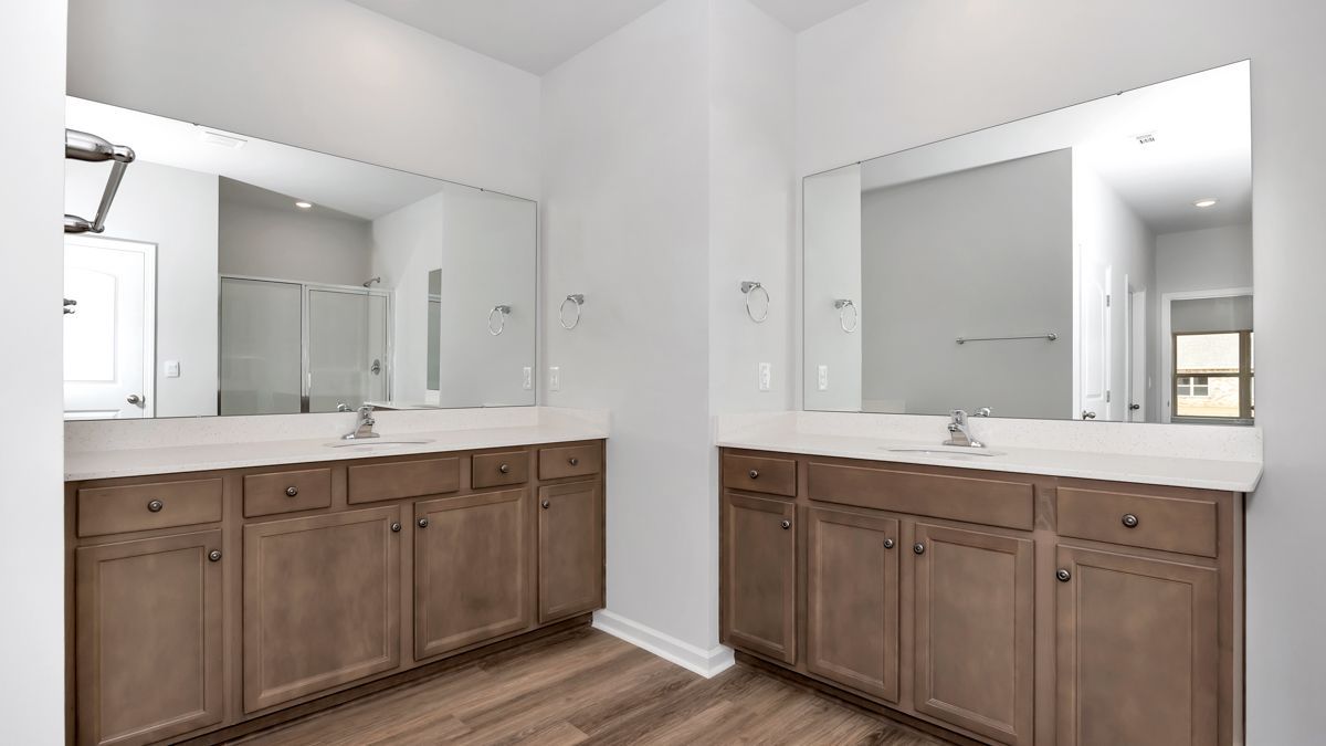 Bathroom with two vanities, large mirrors, light brown cabinets, and wood-look flooring.