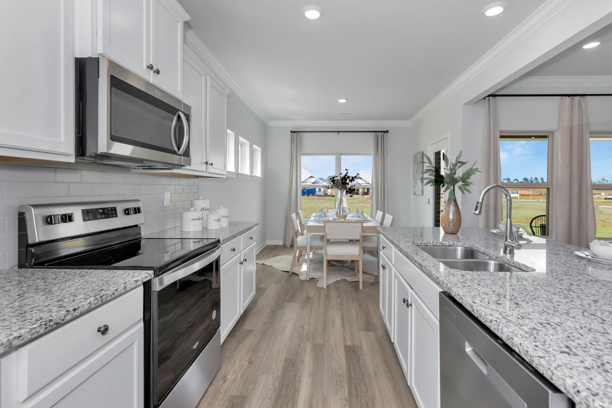 Modern kitchen with white cabinets, stainless steel appliances, and a granite countertop, leading to a dining area.