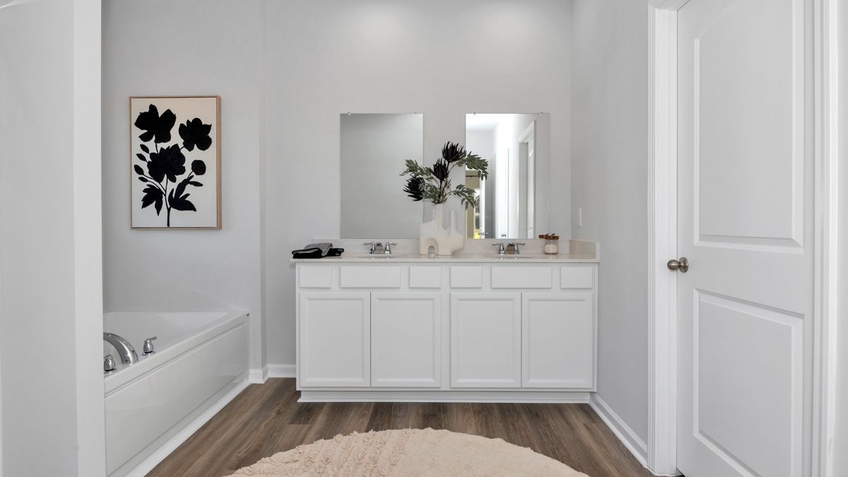 White bathroom with double vanity, artwork, and a bathtub.
