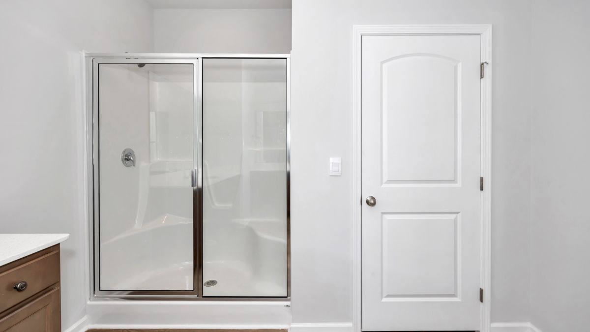 Bathroom with a white shower, a white door, and gray walls.