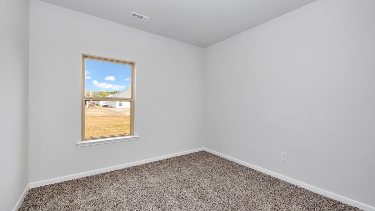 Empty room with gray walls, brown carpet, and a window showing a sunny outdoor view.