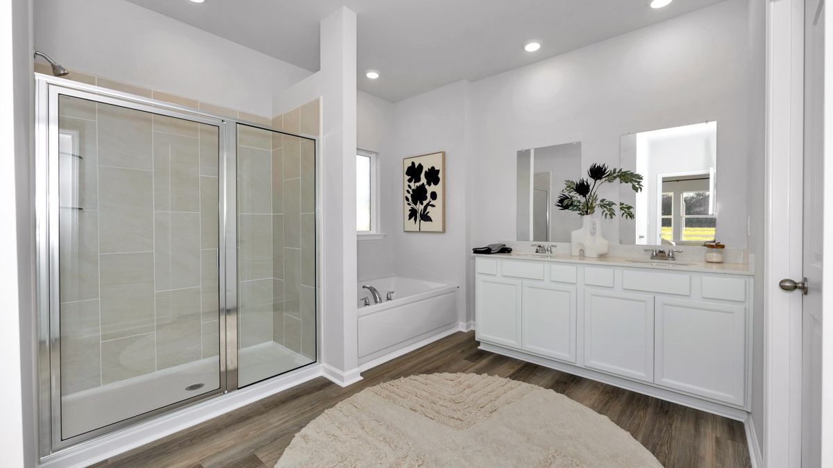 Bright white bathroom with glass shower, vanity, tub, and neutral rug on wood floor.
