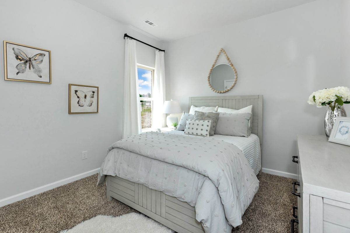 A light-filled bedroom with a bed, rug, and decor in neutral tones.