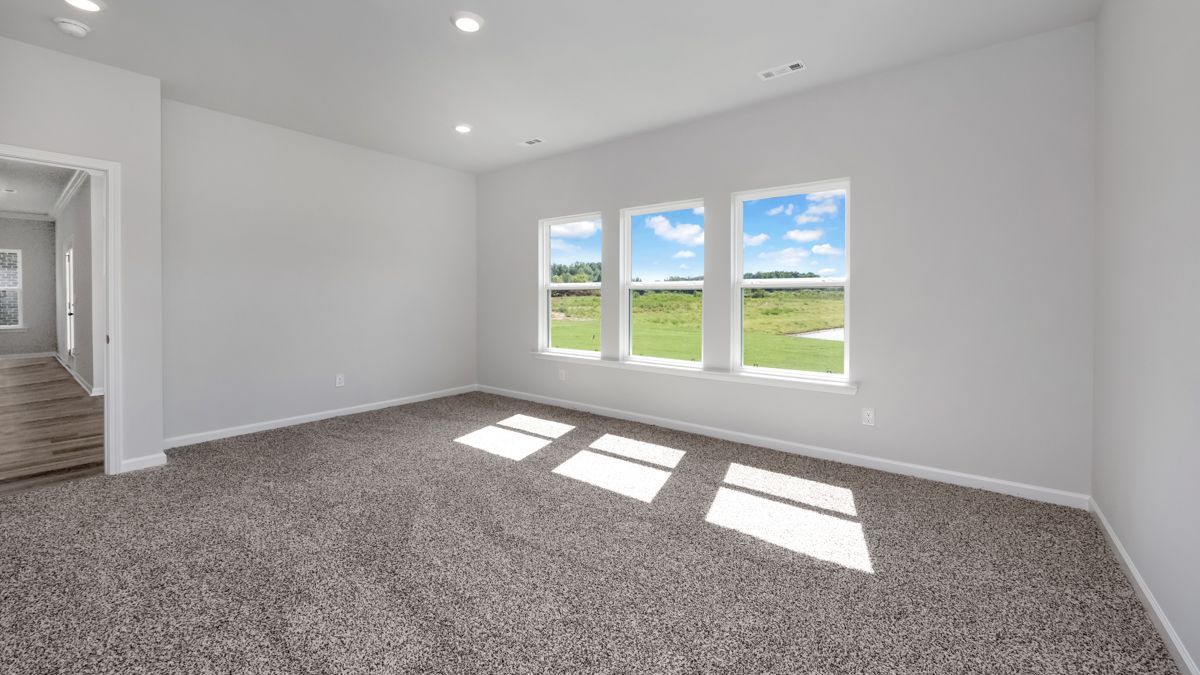 Empty room with carpet, windows facing a green field, and bright sky.