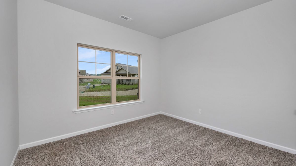 Empty room with carpet, window overlooking a suburban street, and light grey walls.