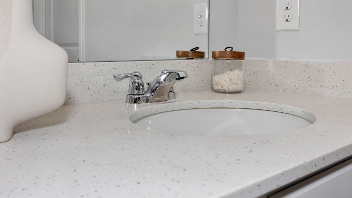 White bathroom sink, faucet, and countertop with a mirror and decorative jar.