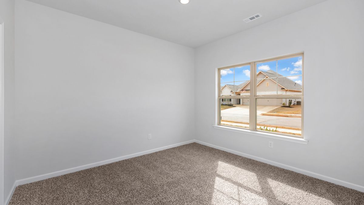 Empty room with white walls, brown carpet, and a window overlooking houses.
