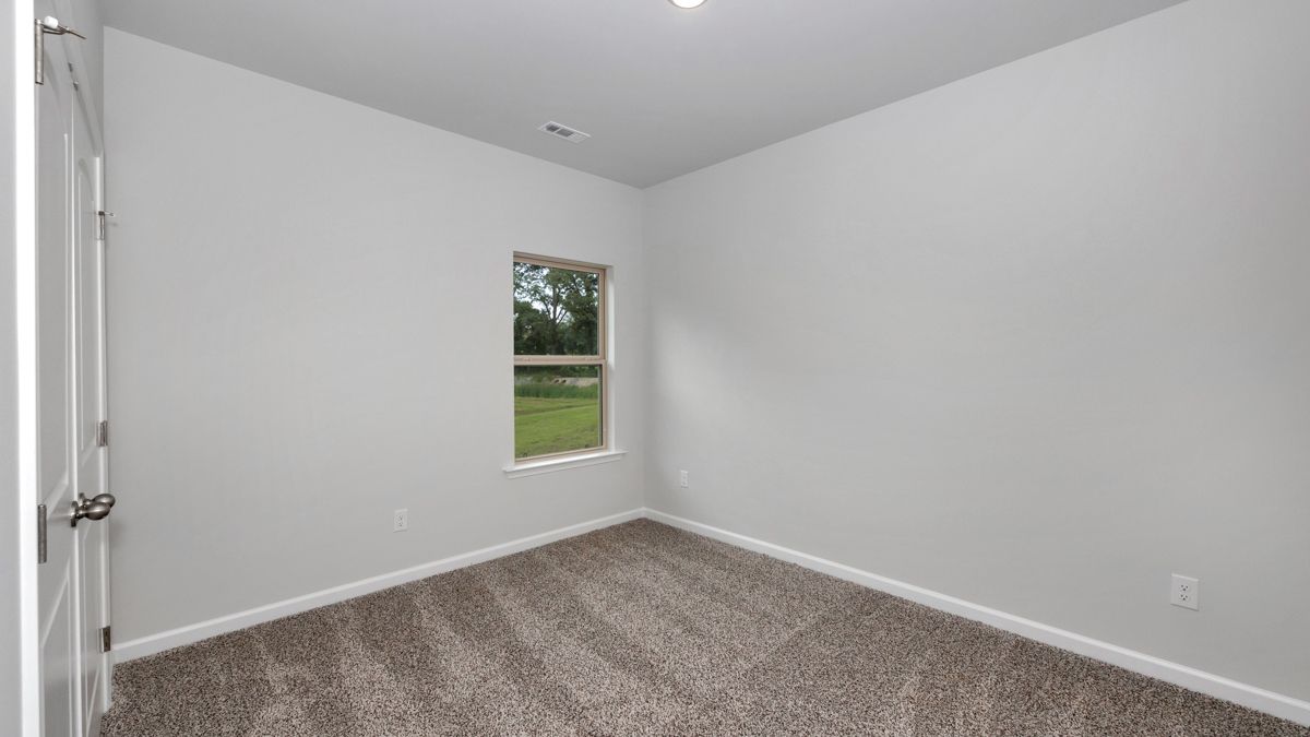 Empty bedroom with gray carpet, white walls, small window, and door.