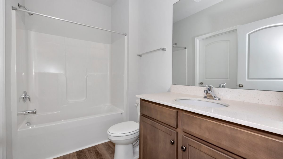 Bathroom with white tub, vanity with brown cabinets, and a closed white door.