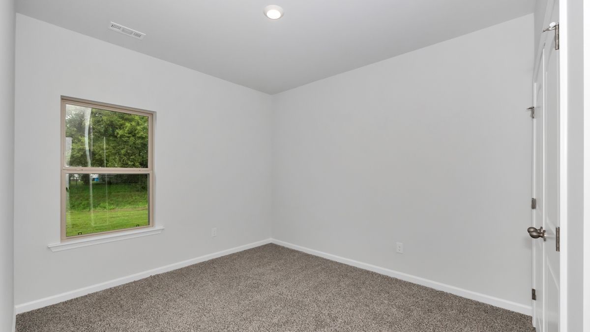 Empty room with window and door. Gray carpet, white walls, and bright light.