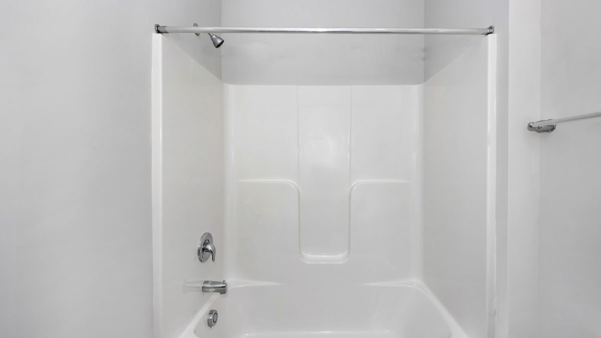 White bathtub and shower stall with chrome fixtures, in a white-walled bathroom.
