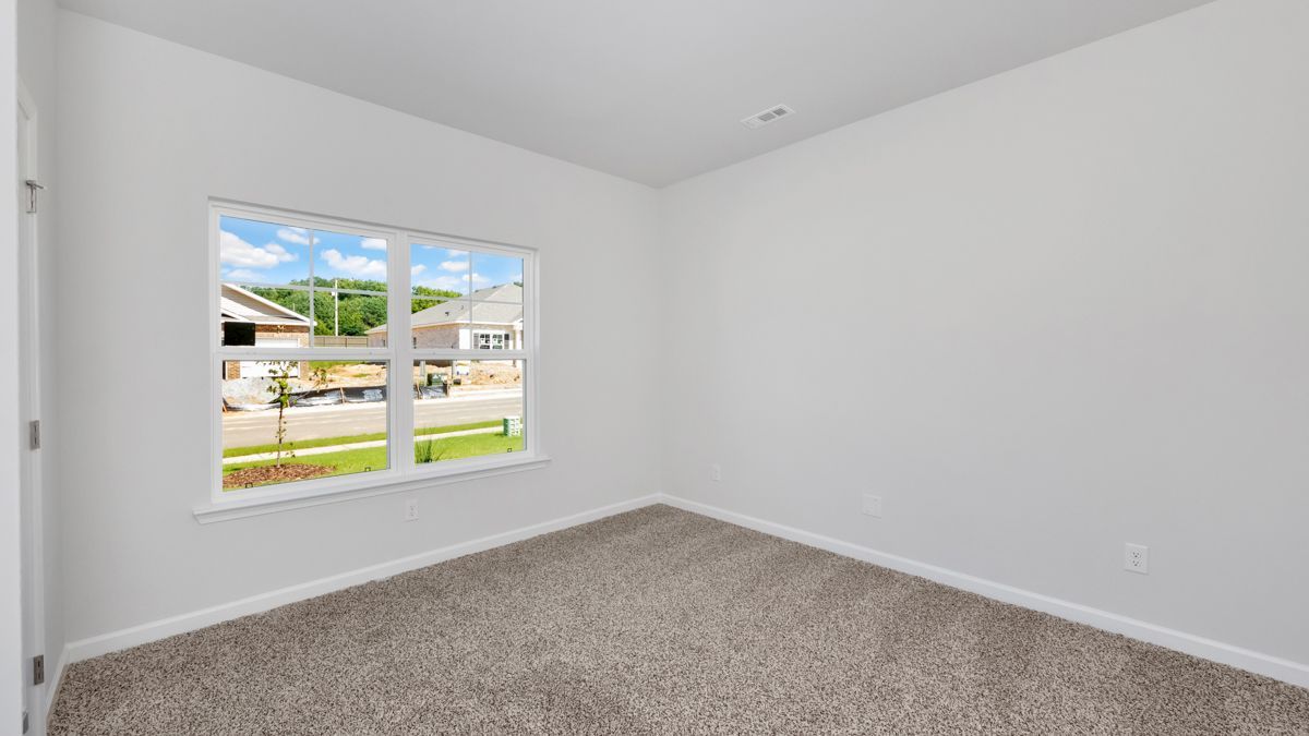Empty bedroom with neutral carpet, white walls, and a window overlooking a neighborhood.