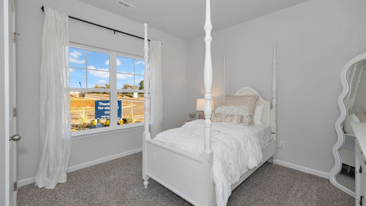 White bedroom with canopy bed, window, and sheer curtains. Gray walls and carpet.