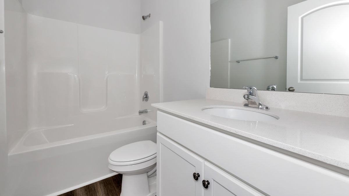 White bathroom with a tub, toilet, vanity with a sink, and a large mirror.