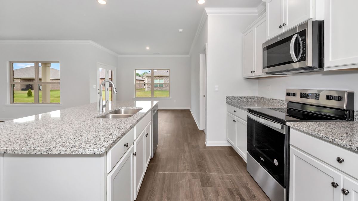 Bright kitchen with white cabinets, granite countertops, stainless steel appliances, and a large island with a sink.