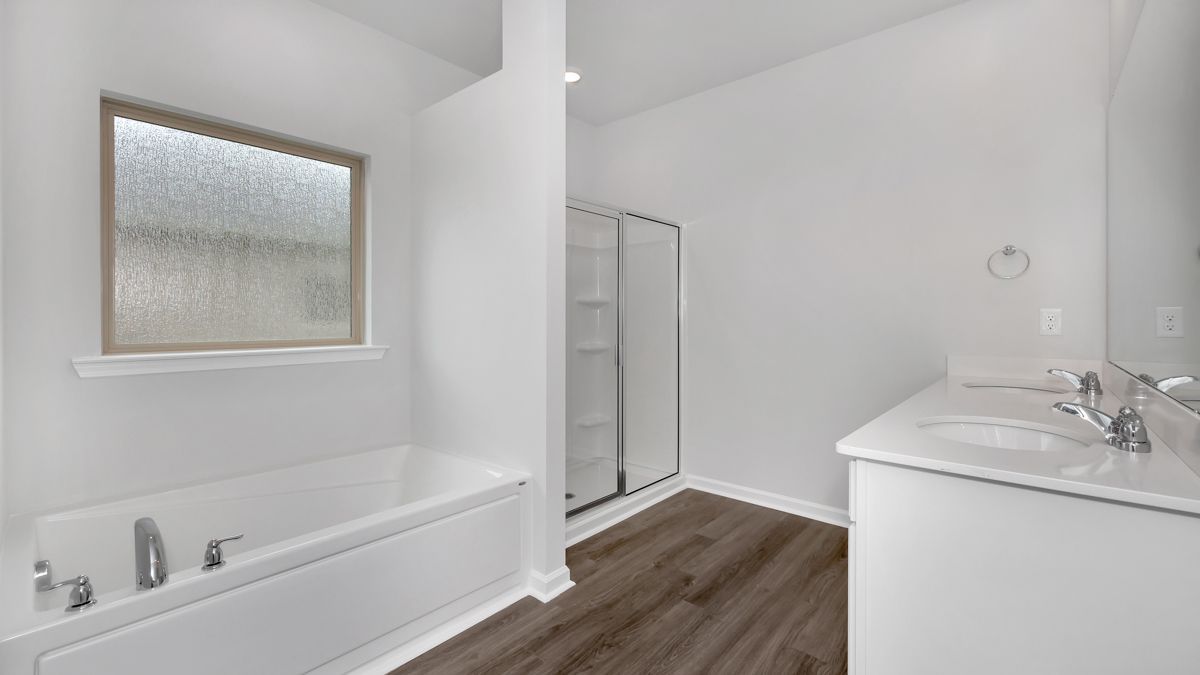 Bright white bathroom with bathtub, shower, vanity, and frosted window. Dark wood-look flooring.