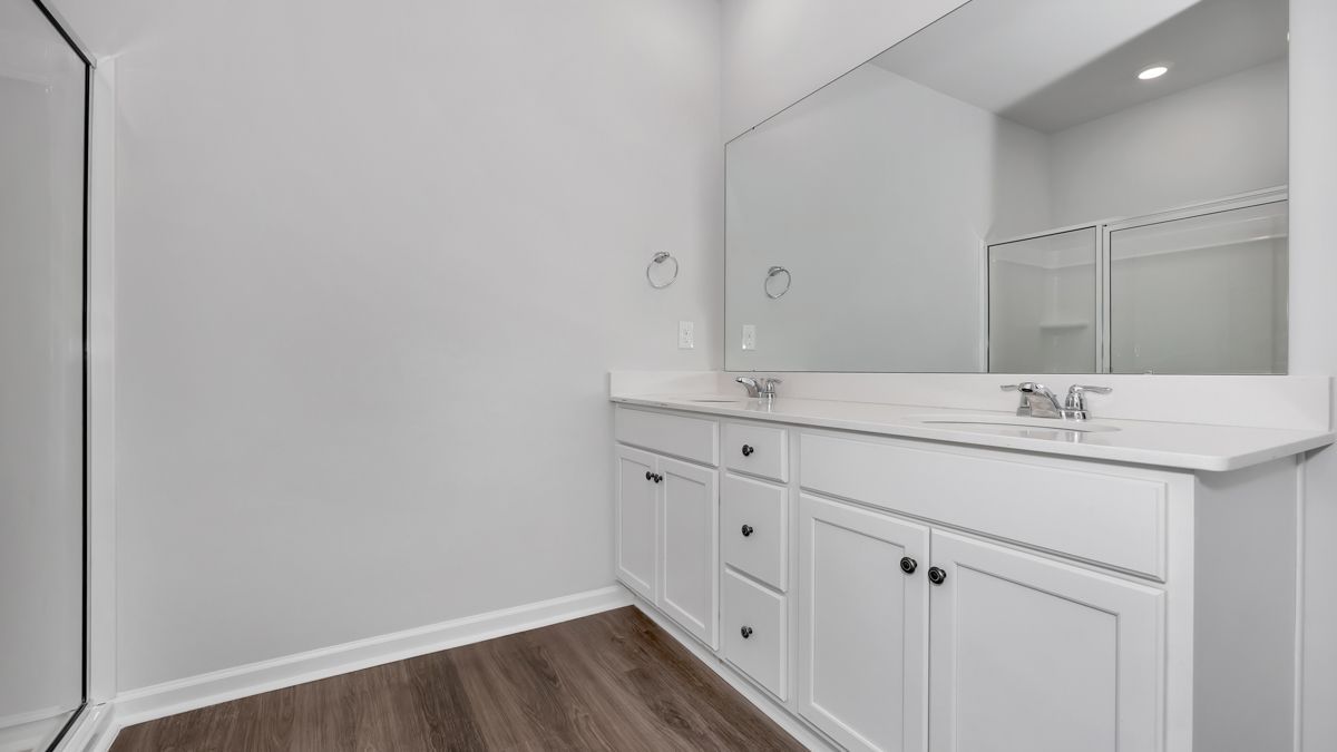 White bathroom with a vanity, mirror, and shower stall.