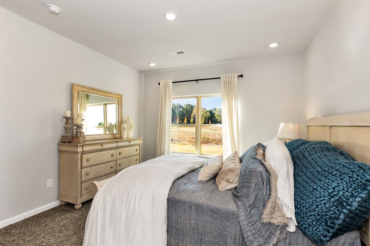 Bedroom with neutral tones, dresser with mirror, and a bed with white and blue bedding, next to a window.
