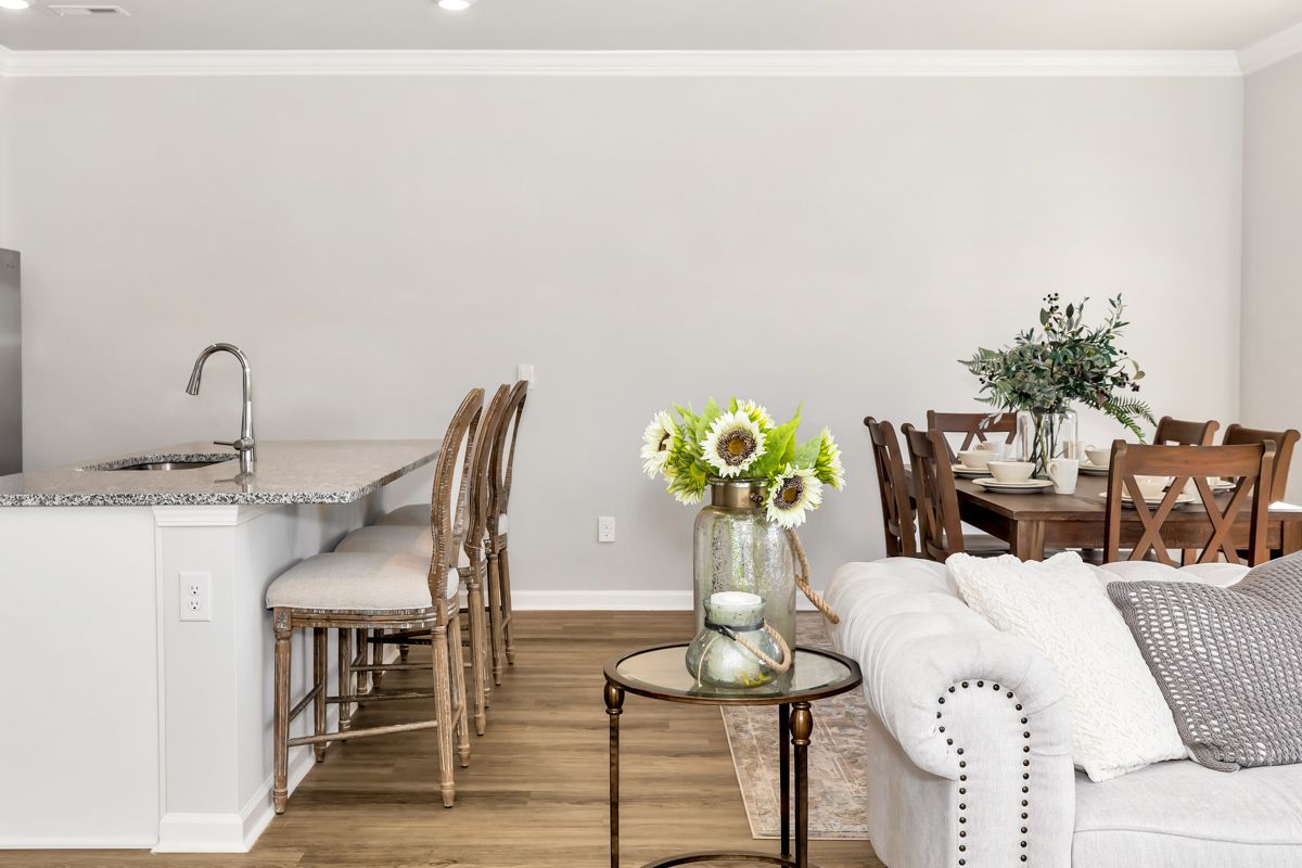 A bright, open-concept living space featuring a kitchen island with stools, dining table, and sofa.